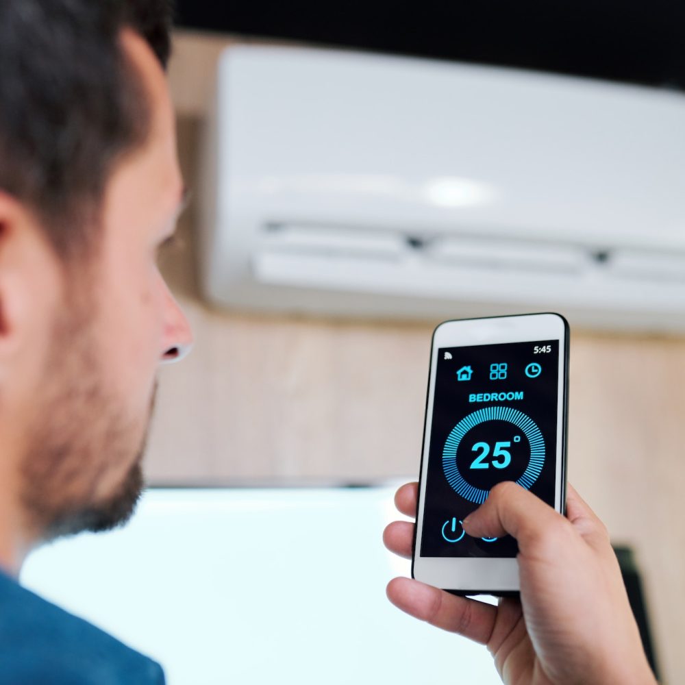 Young man using smart application to adjust temperature of air conditioner